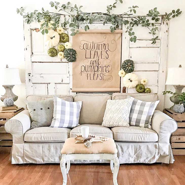 Upholstered coffee table with white base in front of a grey Ikea sofa with check throw pillows with a wall of pumpkins