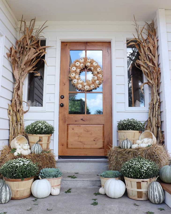 fall front door decor with pumpkin wreath and dried cornstalks 