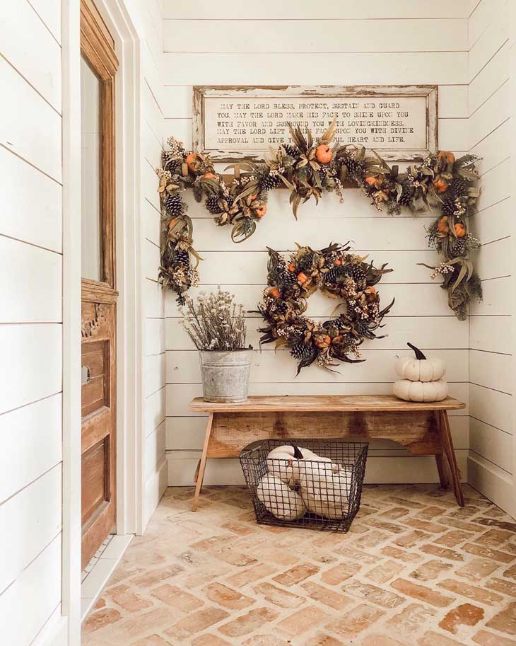 mini pumpkins and pines wreath below fall garland in an entryway