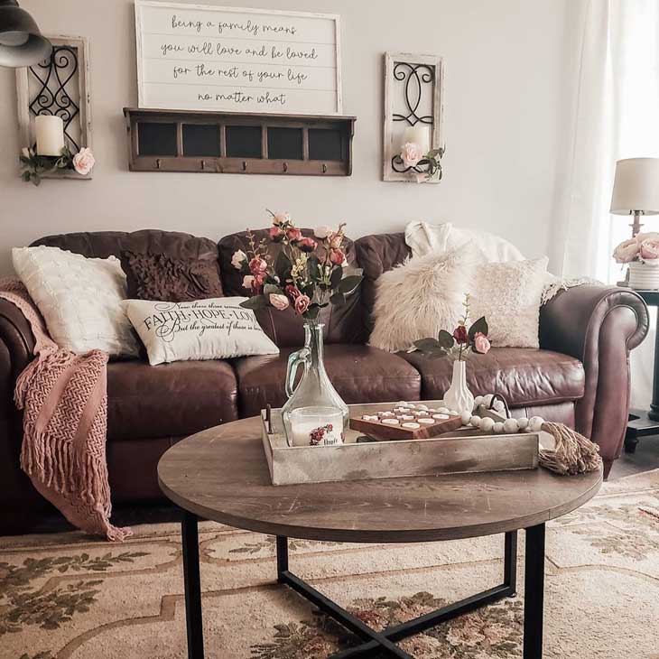 round coffee table with metal legs with wooden tray on it in front of a brown leather sofa