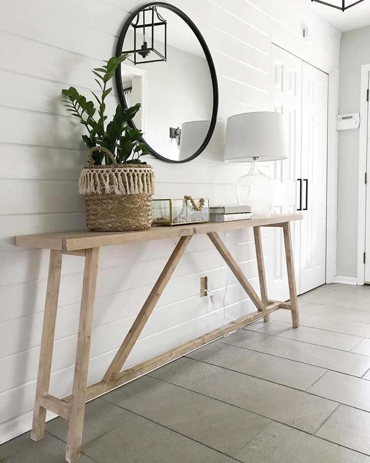 reclaimed wood entryway table with basket and lamp decor and round mirror above it. Slender entry table