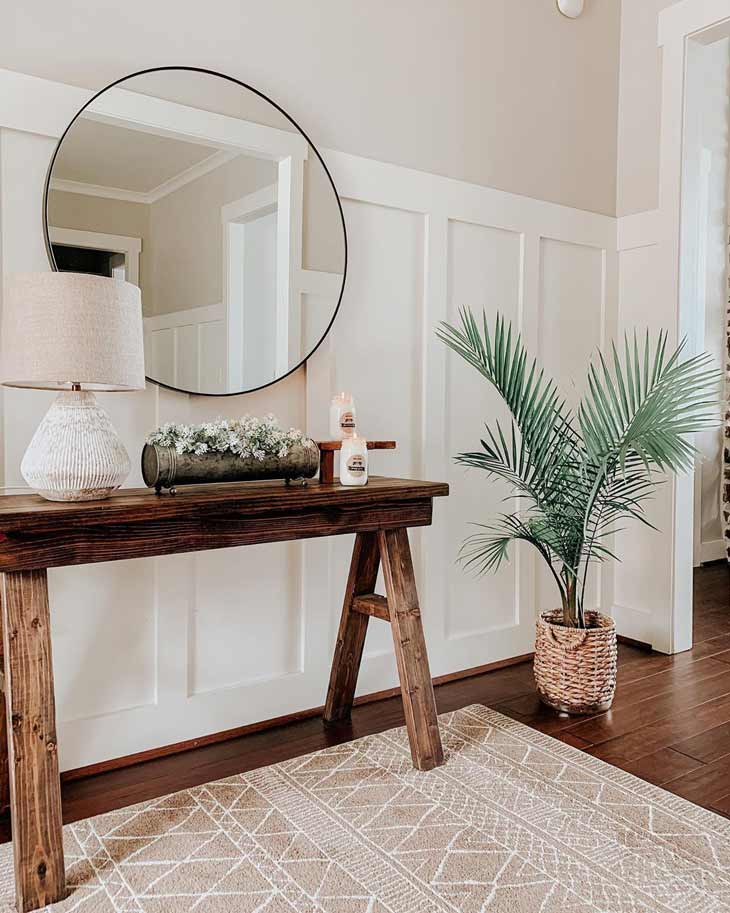 dark wood entryway table with flower decor, table lamp and round mirror