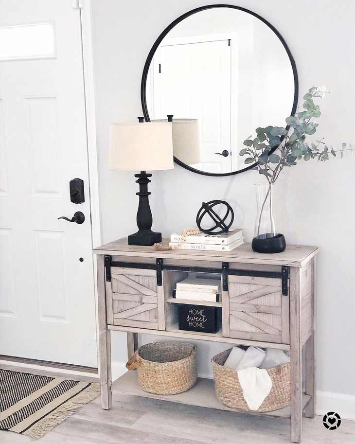 farmhouse style entryway table with black decor accents and round mirror above it