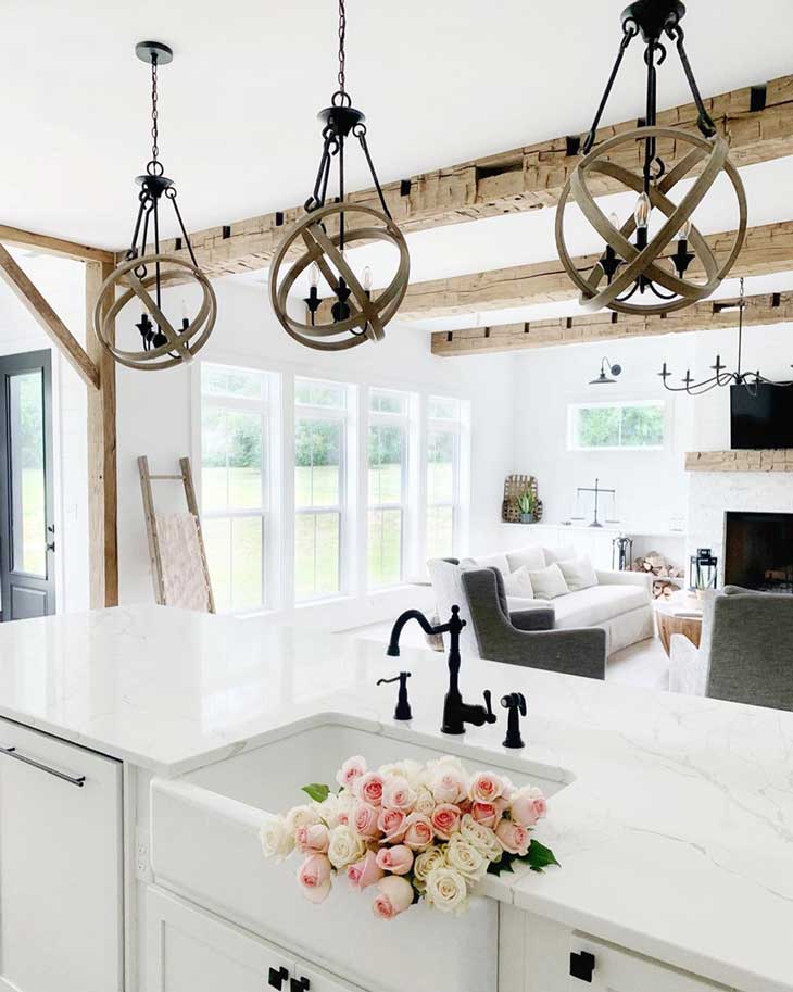 round wood pendant lighting over white kitchen countertop with farmhouse sink in kitchen island and black faucet