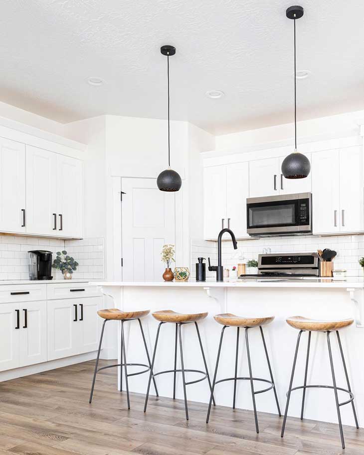 black metal pendant lights over white kitchen island in a white kitchen with black hardware 