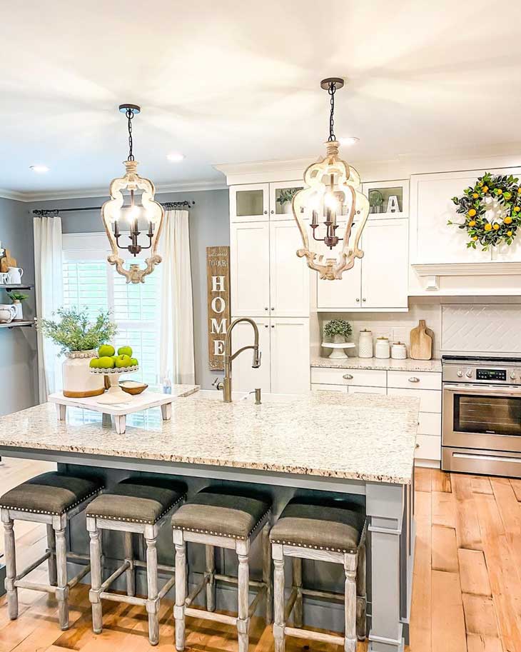 Wood Country-Cottage Chandeliers over grey kitchen island with marble countertop and upholstered bar stools