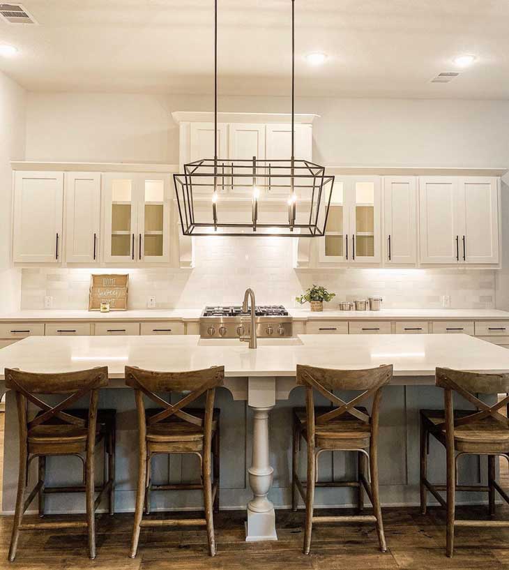 open frame lantern chandelier over kitchen island with white countertop and wood barstools in a white kitchen