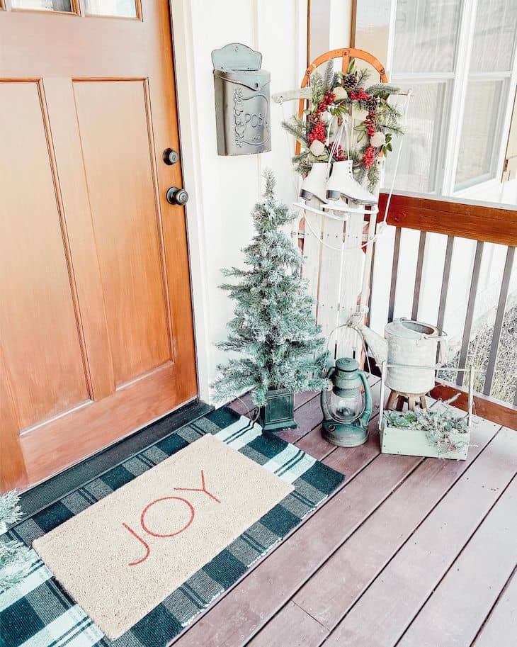 Christmas front door with plaid mat, mini Christmas tree, and antique sled with ice skates