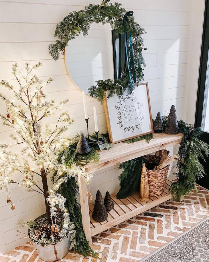 Entry table Christmas decor with big garland, lit tree and round mirror