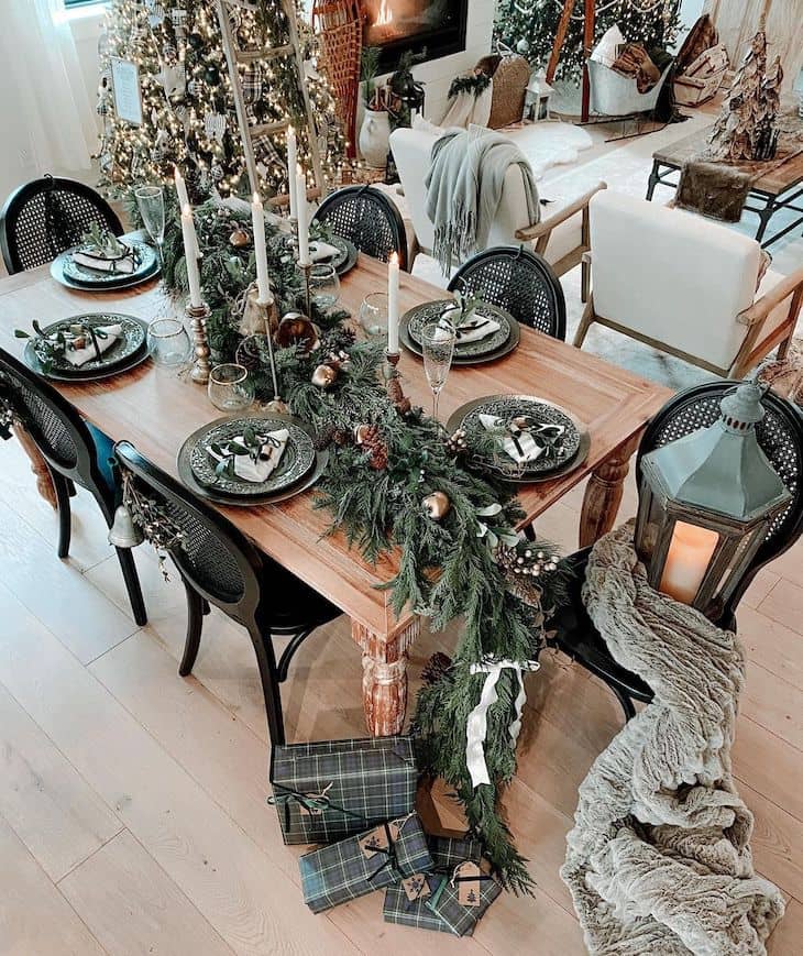 Dining table Christmas decor with big garland and candles. Green and gold Christmas table decor