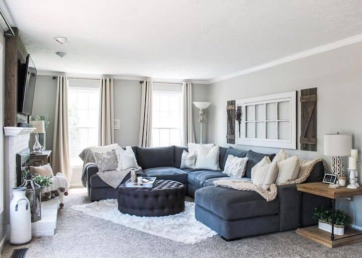 Farmhouse living room with navy blue sectional sofa, grey walls, ottoman as coffee table and over the couch wall decor