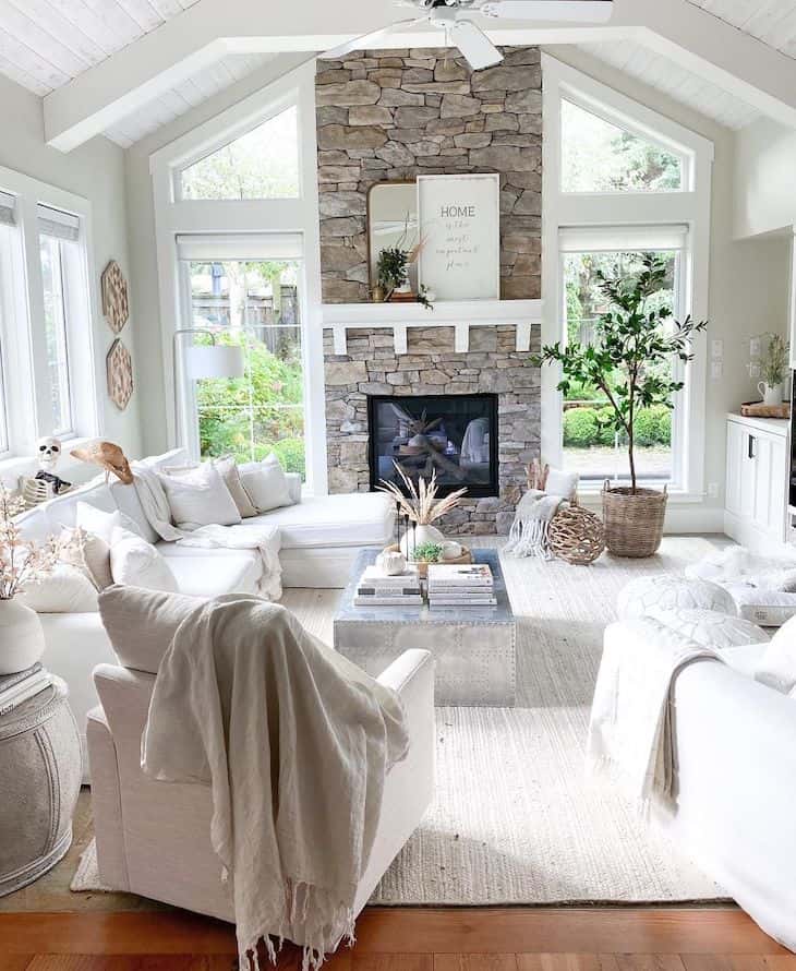 Open concept living room with white beams, stone fireplace, white sectional and windows on each side of fireplace 