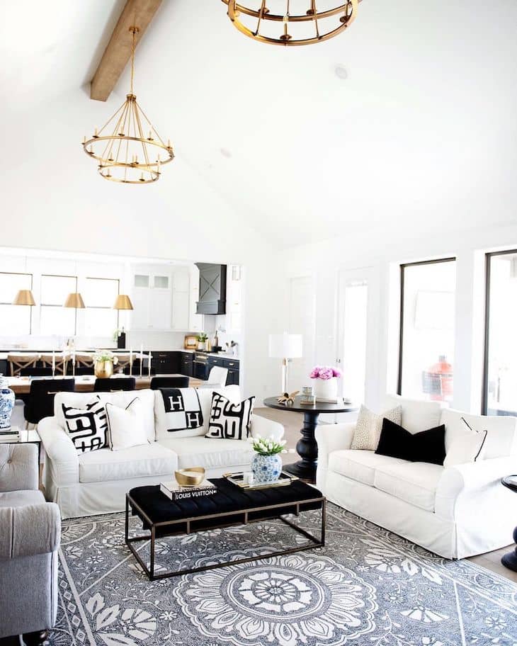 Open concept living room with white couches grey rug and upholstered coffee table