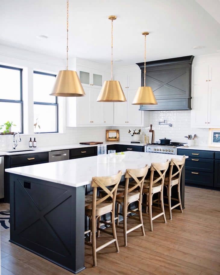 Black kitchen island with wood counter stools and brass kitchen lighting