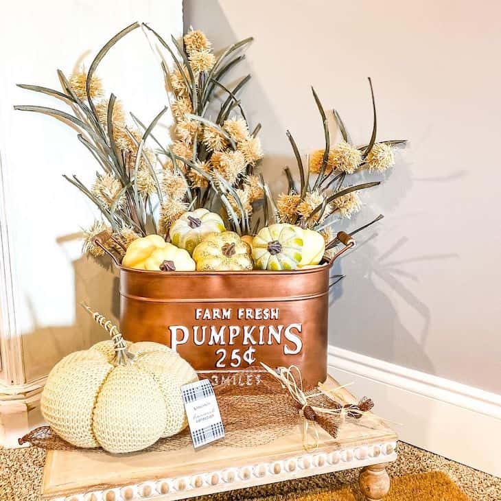 Copper bucket filled with pumpkins and dried stems on a wooden tray