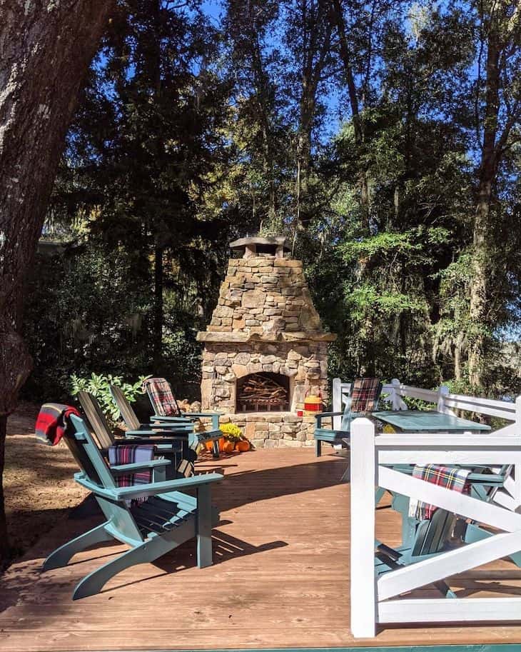 Outdoor deck fireplace in a lake house with Adirondack chairs